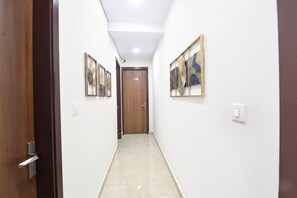A hallway with a wooden door, white walls, and framed artwork. - Fabhotel Tulip Sarover (New Delhi)