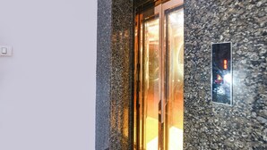 Un ascensor moderno con puerta de vidrio, ubicado en un edificio con fachada de piedra moteada.