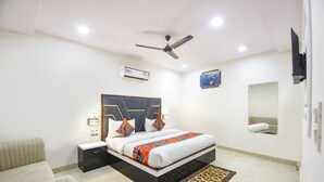 Una habitación de hotel moderna con una cama, mesitas de noche, ventilador de techo, equipo de aire acondicionado, un cuadro, un espejo y una alfombra estampada.