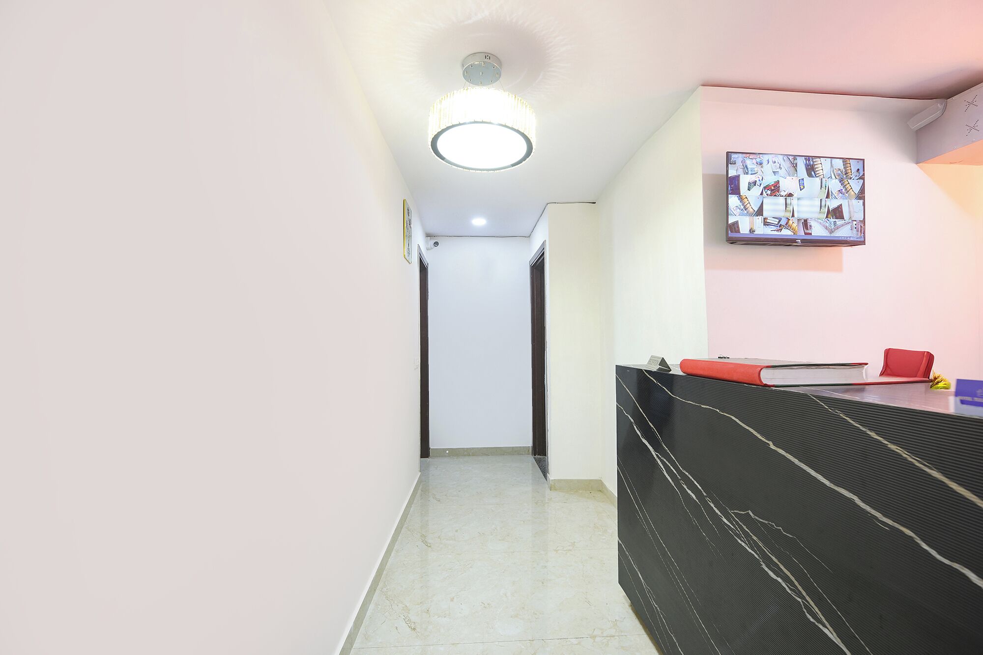 A hallway with a ceiling light, a door, a television mounted on the wall, and a sofa with a book and a red cushion.