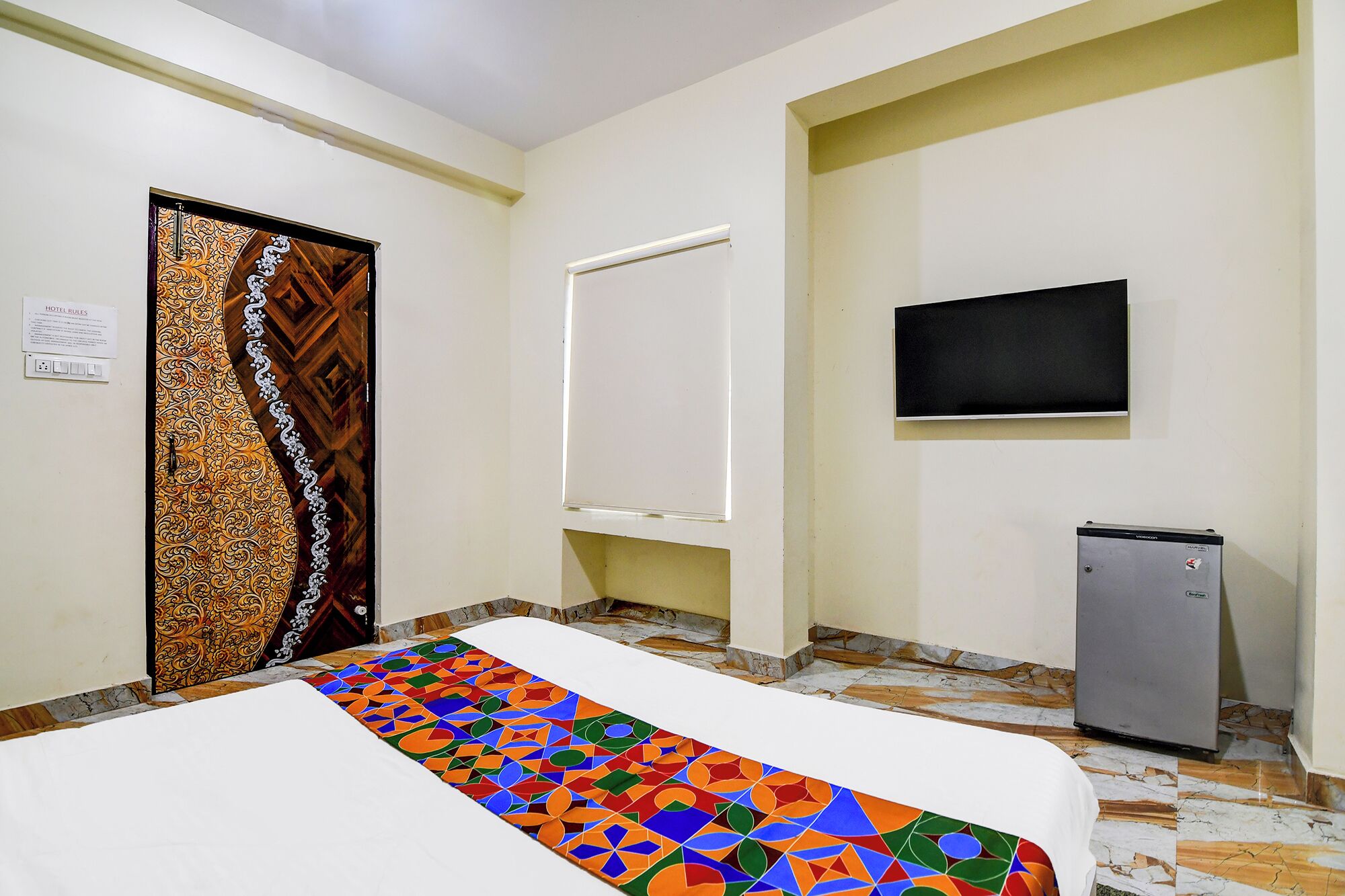 Ein Hotelzimmer mit Bett, Fernseher, kleinem Kühlschrank und einer Tür mit Muster.