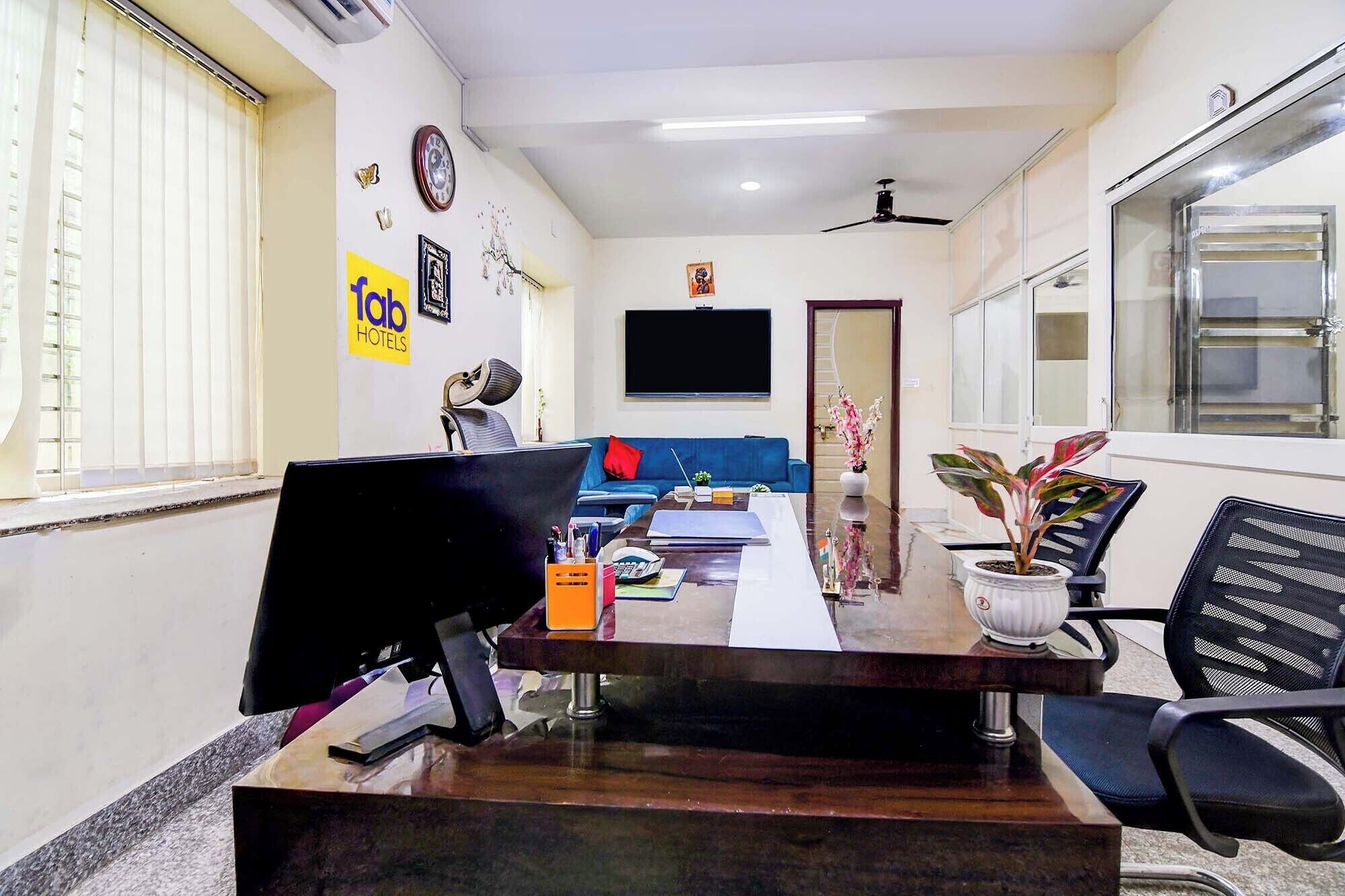 A hotel room with a desk, chairs, a television, a sofa, and a window.