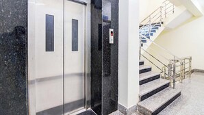 Um elevador com visor digital, ao lado de uma escadaria com grades de metal e degraus de granito.