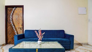 Uma sala de estar com um sofá azul, uma mesa de centro de vidro e um arranjo floral.