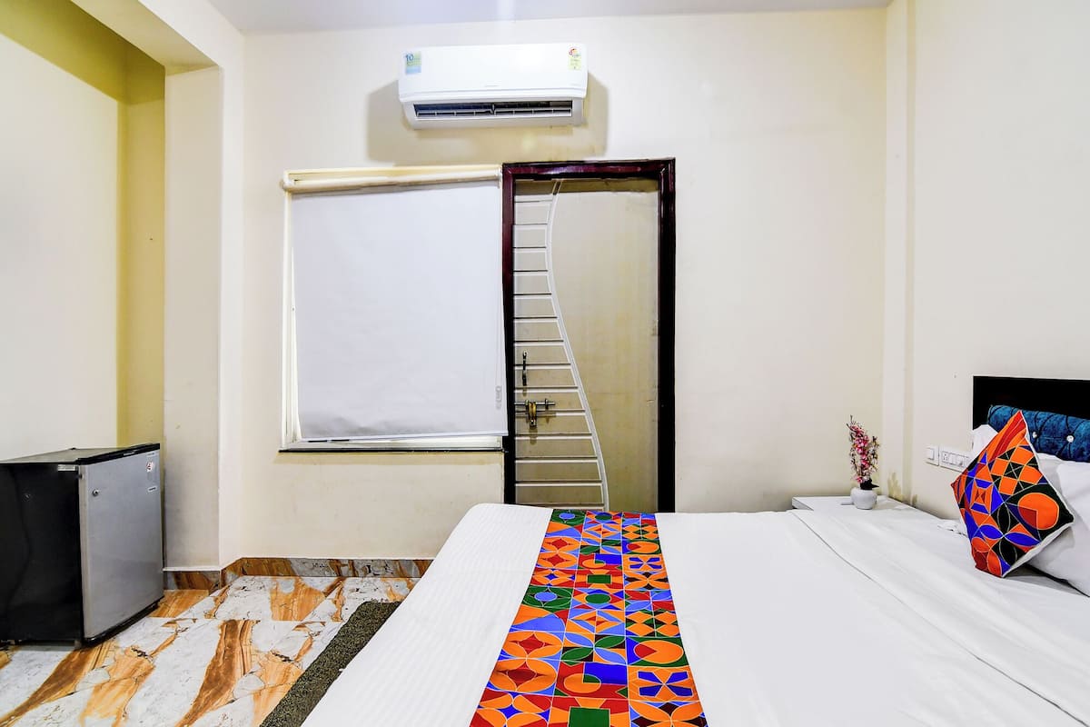 A hotel room with a bed, a small desk, a refrigerator, a window with a view, and an air conditioning unit.