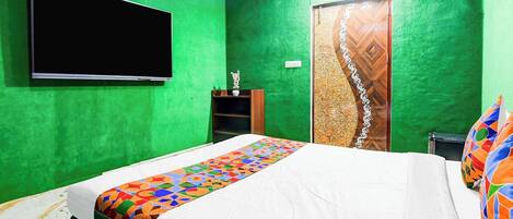 A room with green walls, a bed with a colorful bedspread, a TV mounted on the wall, and a wooden door with a decorative panel.