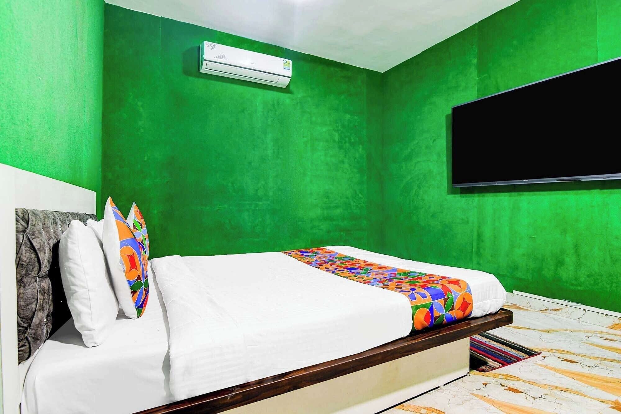 A bedroom with green walls, a bed with white bedding and colorful pillows, an air conditioner, and a TV mounted on the wall.