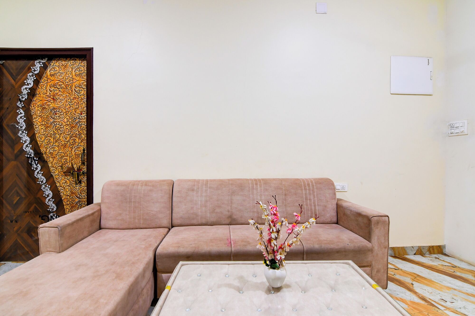 A living room with a beige sofa, a white coffee table, and a vase with flowers.