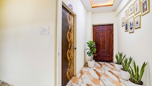 Um corredor com porta de madeira, planta em vaso e quadros na parede.