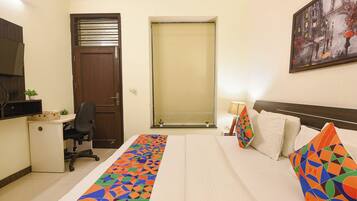 A hotel room with a bed, a desk, a chair, a TV, and a painting on the wall.