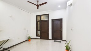 A spacious room with white walls, two wooden doors, a ceiling fan, and potted plants.