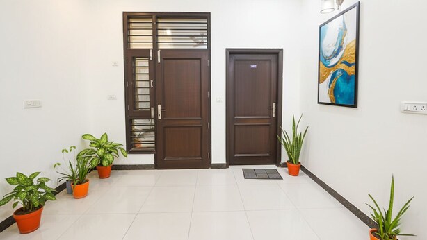 A clean, modern entrance with two wooden doors, potted plants, and a framed artwork on the wall.