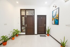 A clean, modern entrance with two wooden doors, potted plants, and a framed artwork on the wall. - FabHotel Golf Luxury (Gurugram)