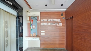 Un espace d’accueil d’hôtel comprenant un comptoir de réception en bois, un panneau d’information fixé au mur et une caméra de surveillance.