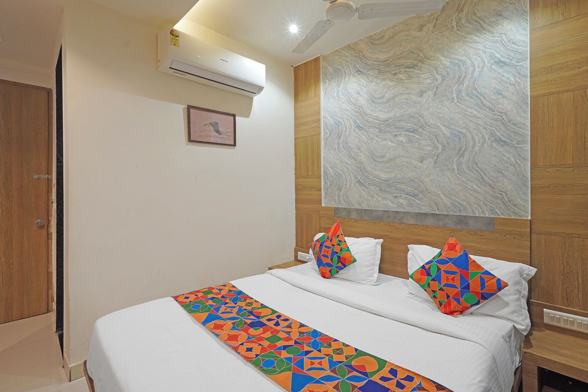 A hotel room with a bed, a wooden headboard, a marble wall, and an air conditioning unit.
