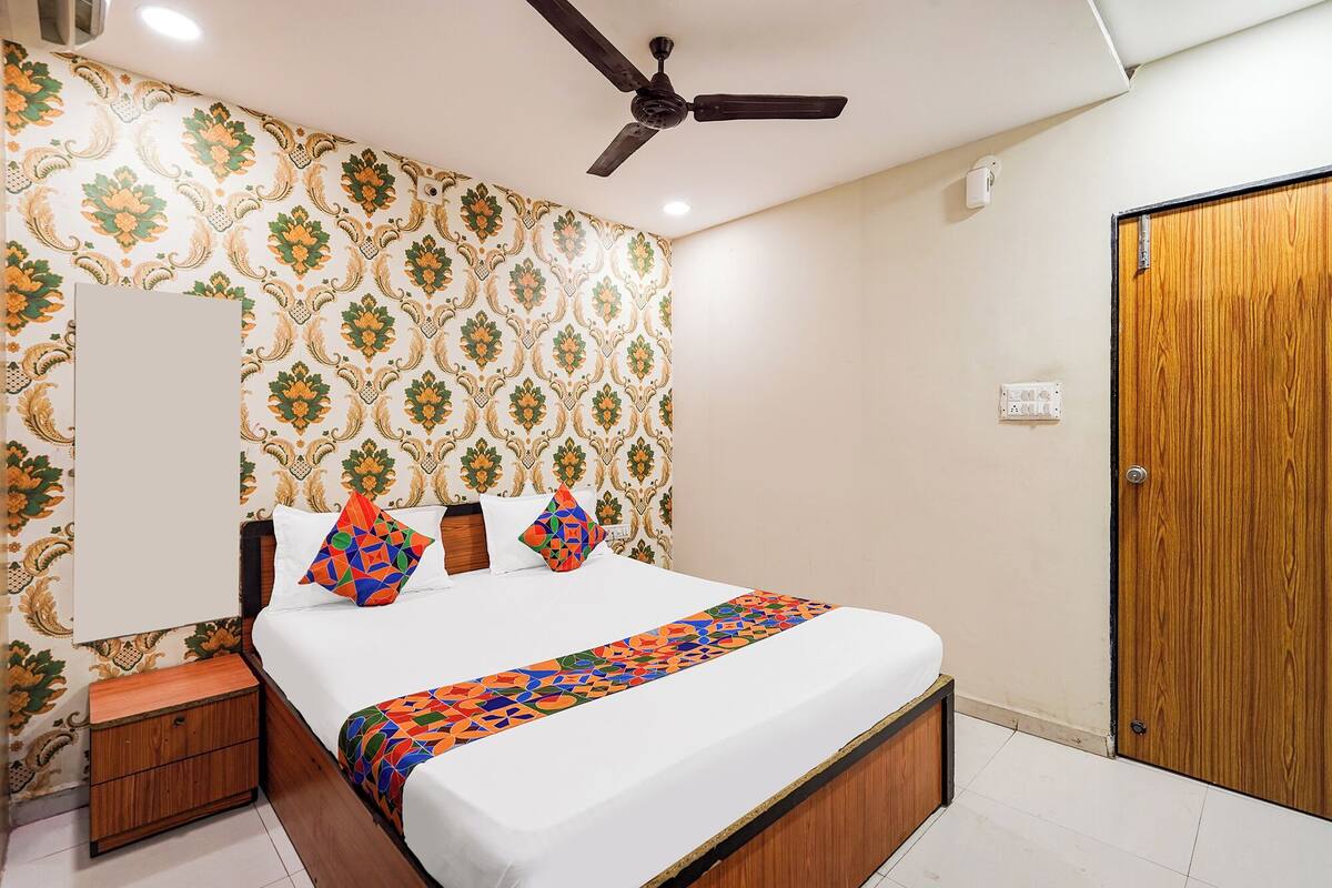 A bedroom with a bed, a nightstand, a wooden wardrobe, a ceiling fan, and patterned wallpaper.