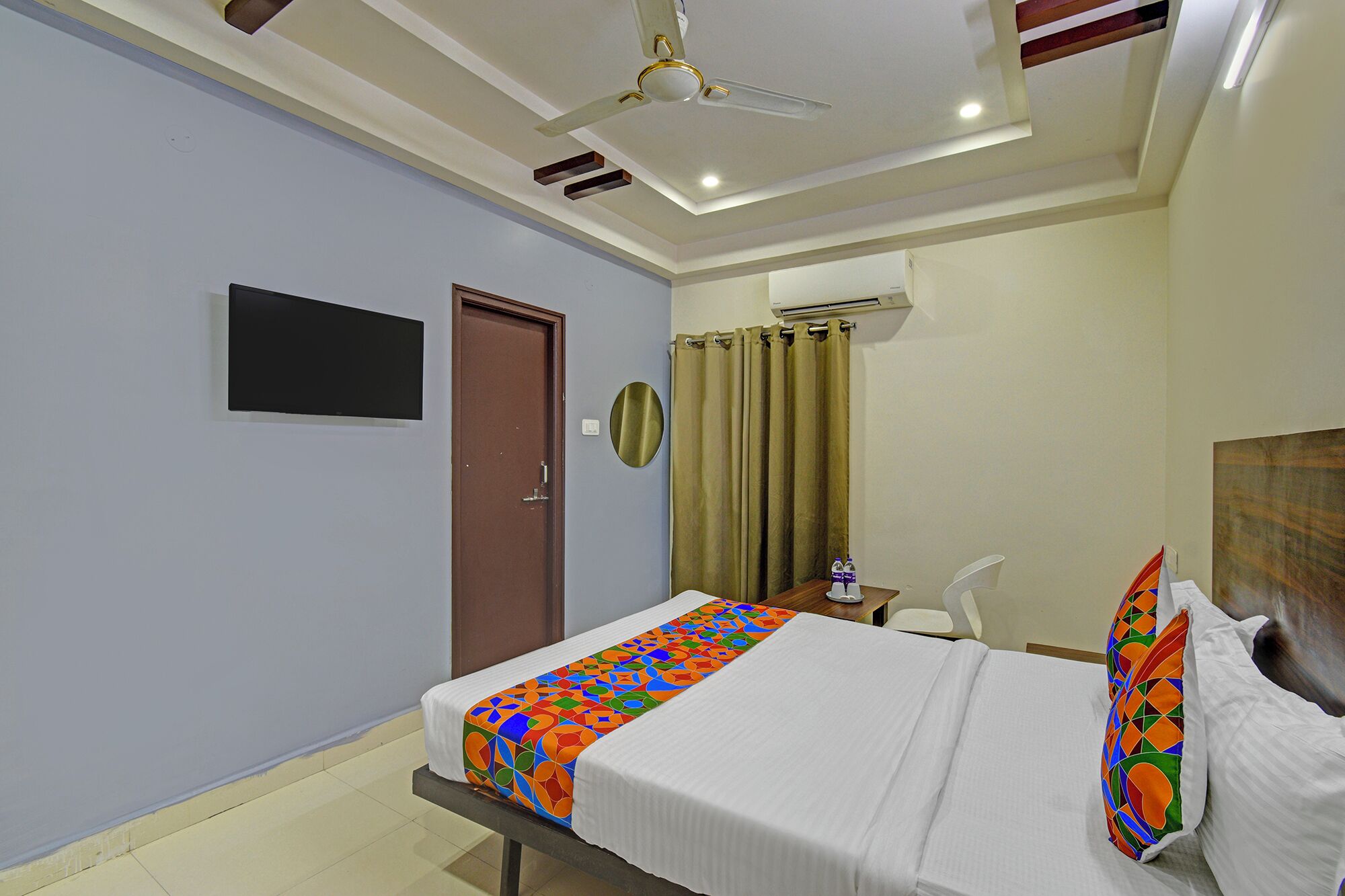 Une chambre d’hôtel équipée d’un lit, d’un ventilateur de plafond, d’un téléviseur à écran plat, d’un appareil de climatisation et d’un rideau.