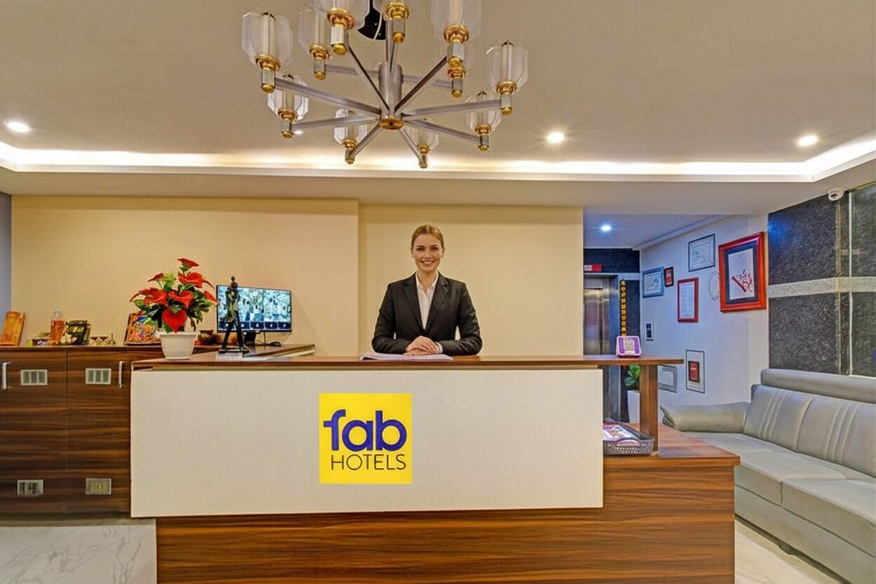 En receptionsdisk med 'fab hotels'-logo, en moderne lysekrone og et siddeområde med sofa og billedkunst på væggen.