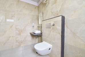 Une salle de bain moderne avec un sol en marbre, des toilettes blanches, un lavabo avec un distributeur de savon et un espace douche.