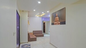 A hallway with a brown sofa, a patterned rug, and a Buddha statue on the wall. - Fabhotel Rajtilak (Ahmedabad)