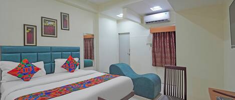A hotel room with a bed, a desk, a chair, a ceiling fan, and an air conditioning unit.