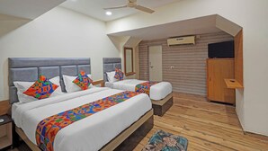 A hotel room with two beds, a ceiling fan, an air conditioning unit, a television, and a wooden wardrobe. - Fabhotel Rajtilak (Ahmedabad)