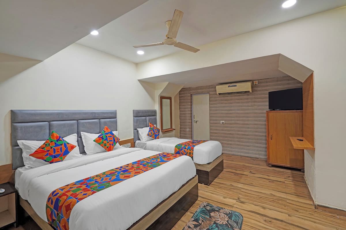 Une chambre d’hôtel avec deux lits, un ventilateur de plafond, un appareil de climatisation, une télévision et une armoire en bois.