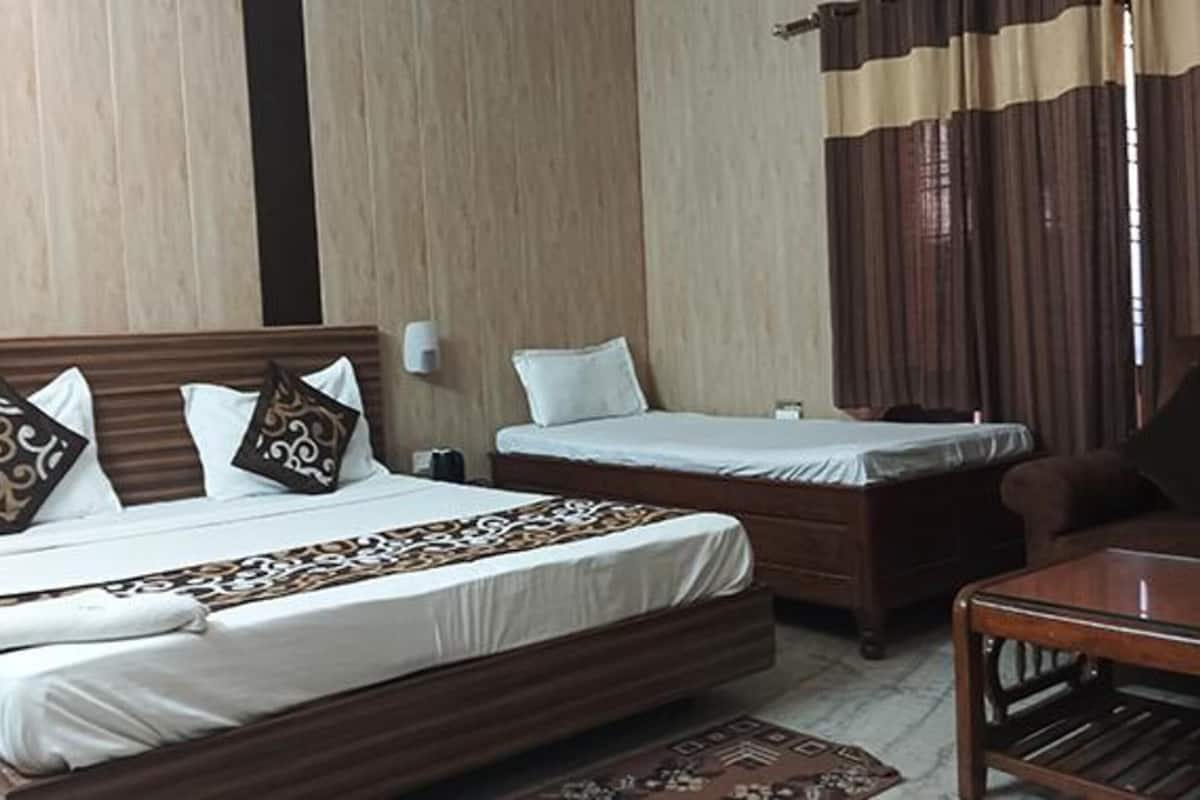 A hotel room with two beds, a wooden headboard, a bedside table, a nightstand, and a patterned rug.