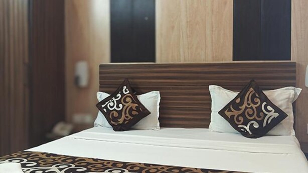 A hotel room with a wooden headboard, two decorative pillows, and a patterned bedspread. - Fabhotel Crown Inn (Lucknow)