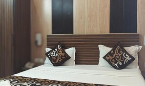 A hotel room with a wooden headboard, two decorative pillows, and a patterned bedspread. - Fabhotel Crown Inn (Lucknow)
