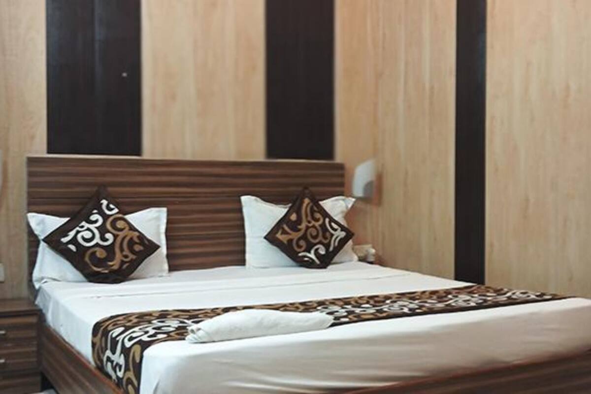 A neatly made bed with patterned pillows and a decorative throw, set against a wooden headboard and wall paneling.