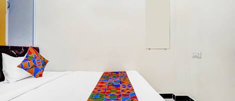 A hotel room with a bed, a colorful geometric-patterned runner, a plain wall, and a small whiteboard.