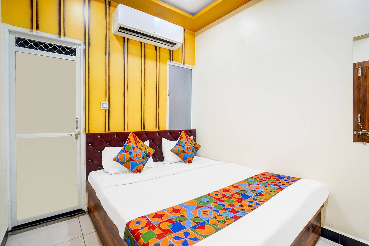 A hotel room with a bed, a window, an air conditioning unit, and a door.
