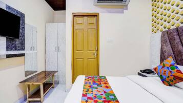 Un dormitorio con cama, una puerta de madera, un televisor montado en la pared y un equipo de aire acondicionado.