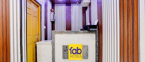 A hotel reception area with a marble counter, a ceiling fan, and vertical wooden paneling.