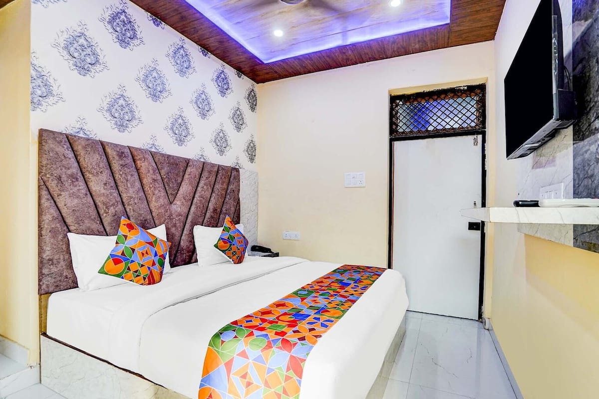 A bedroom with a bed, patterned wallpaper, a wooden headboard, and a ceiling light fixture.