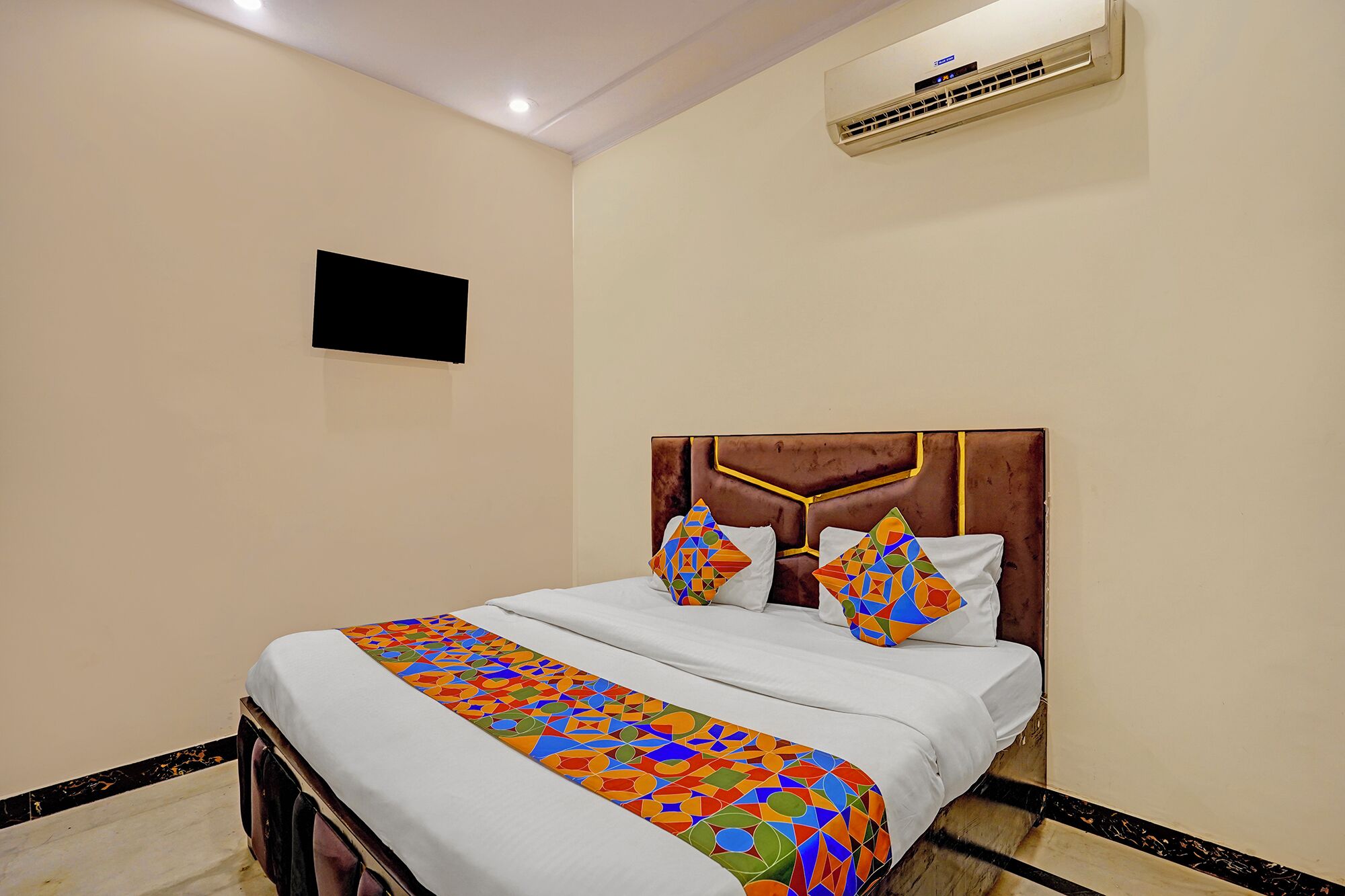 A hotel room with a bed, a headboard, and an air conditioning unit on the wall.