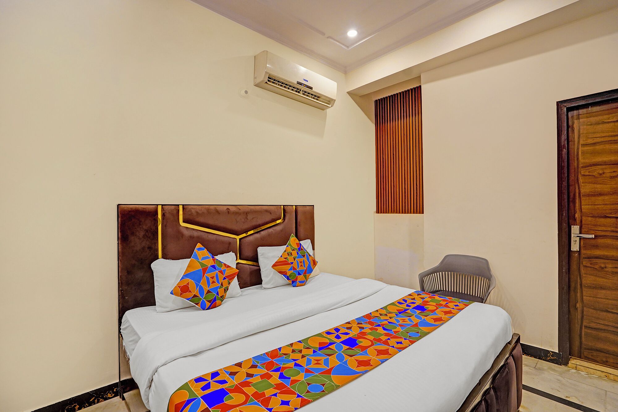 A neatly made bed with a patterned bedspread, a headboard with a geometric design, and an air conditioning unit mounted on the wall.