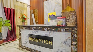 A reception desk with a marble top, a 'RECEPTION' sign, a wooden panel wall, a Buddha statue, and a potted plant. - Fabhotel Rn Residency (Ghaziabad)
