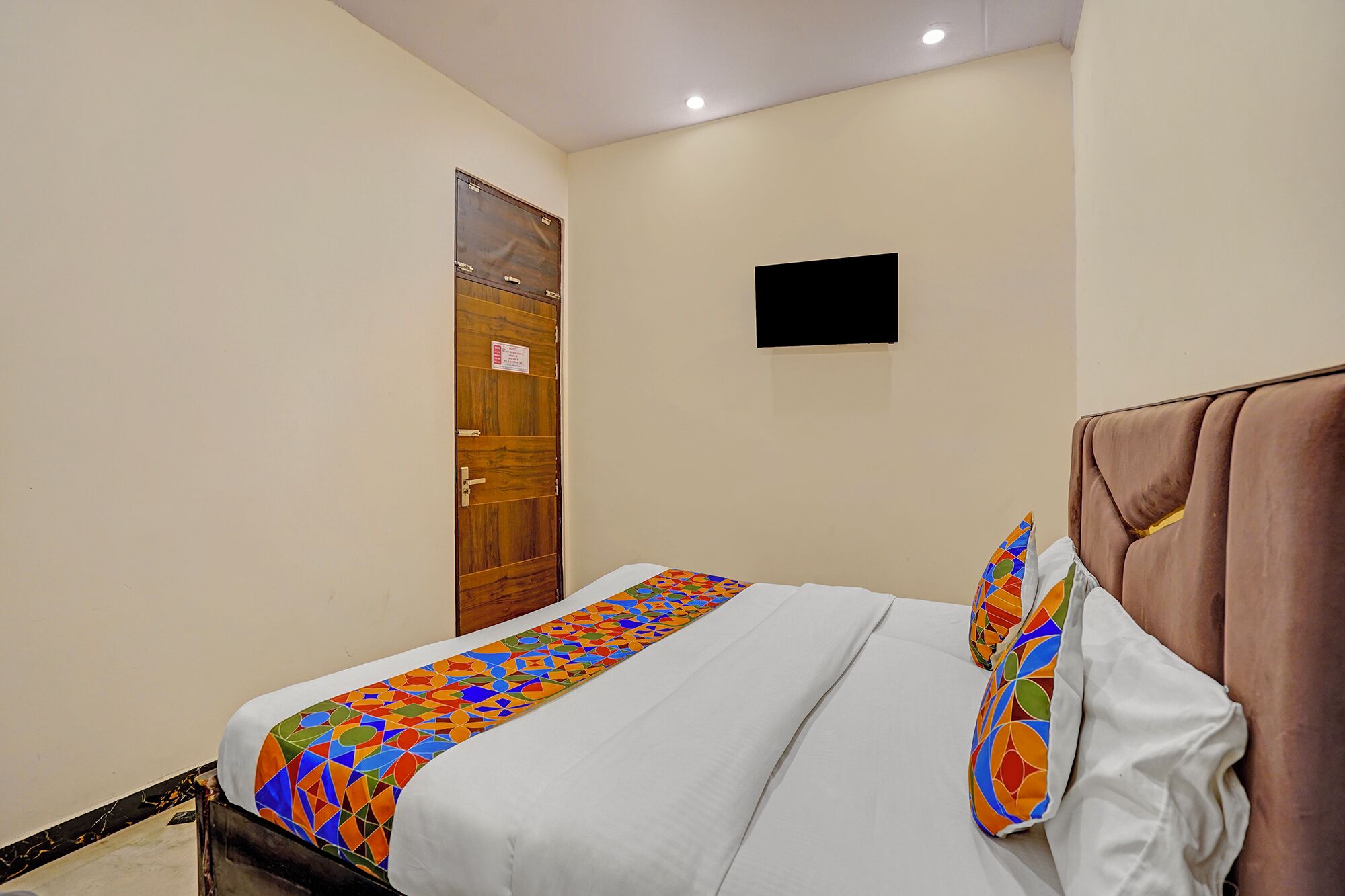 Een hotelkamer met een bed, een houten deur en een flatscreen televisie aan de muur.