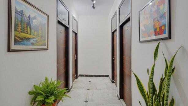 A hallway with wooden doors, framed paintings, and potted plants. - Fabhotel Rn Residency (Ghaziabad)