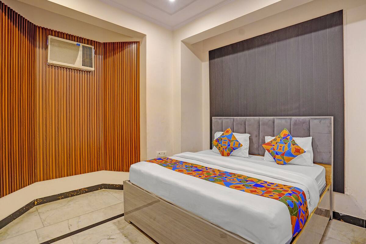 A hotel room with a bed, a wooden panel wall, a large window, and a ceiling vent.