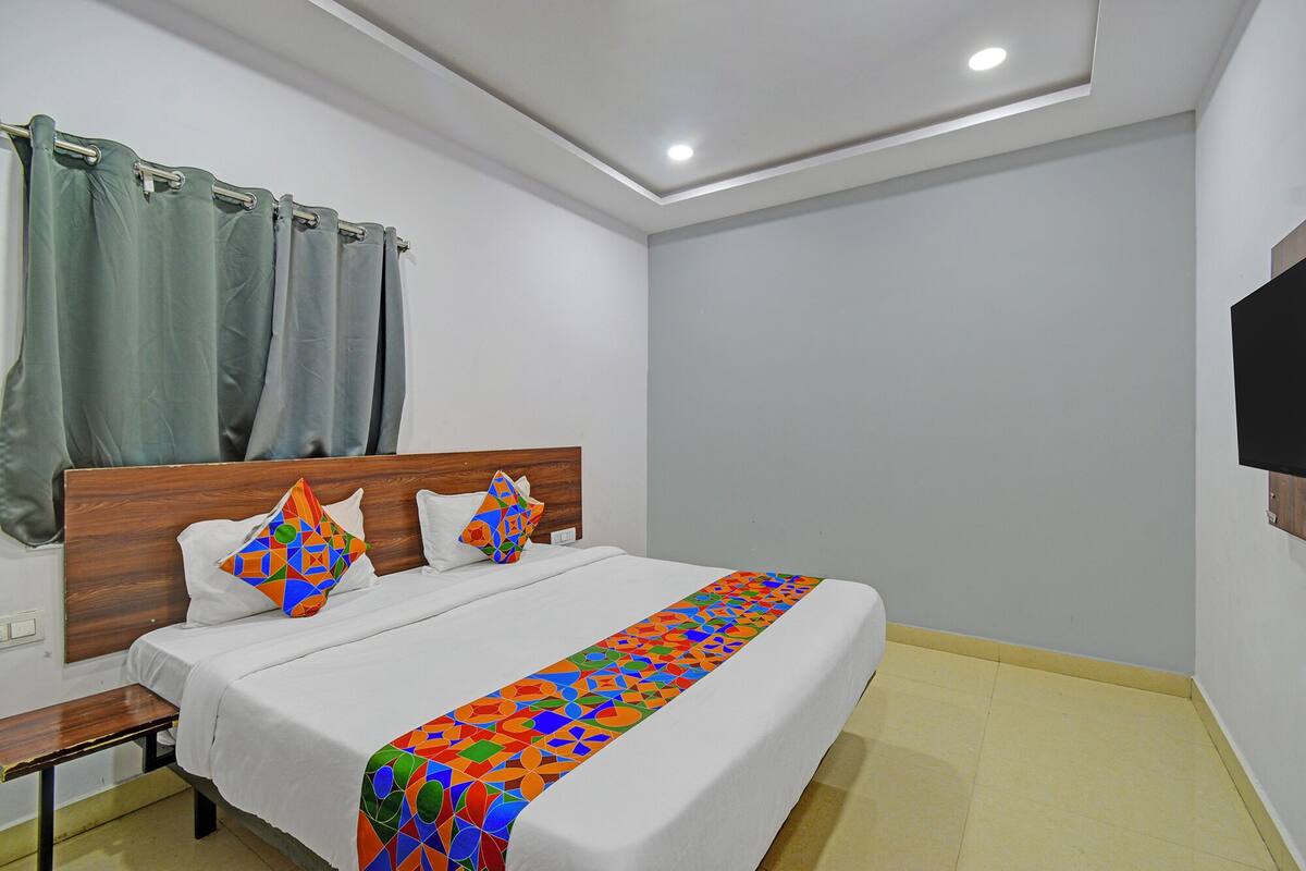 Habitación de hotel con una cama, mesita de noche, televisor montado en la pared y ventana con cortinas.