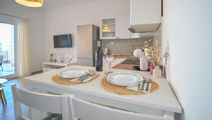 A modern kitchen with white cabinetry, a dining table set with plates, cutlery, and a bottle. - AMI Apartment Strožanac (Podstrana)