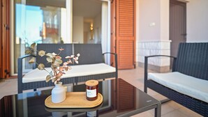 A glass-top table with a white vase and a jar of jam, a wicker sofa, and a wooden door in a room with a view. - AMI Apartment Strožanac (Podstrana)