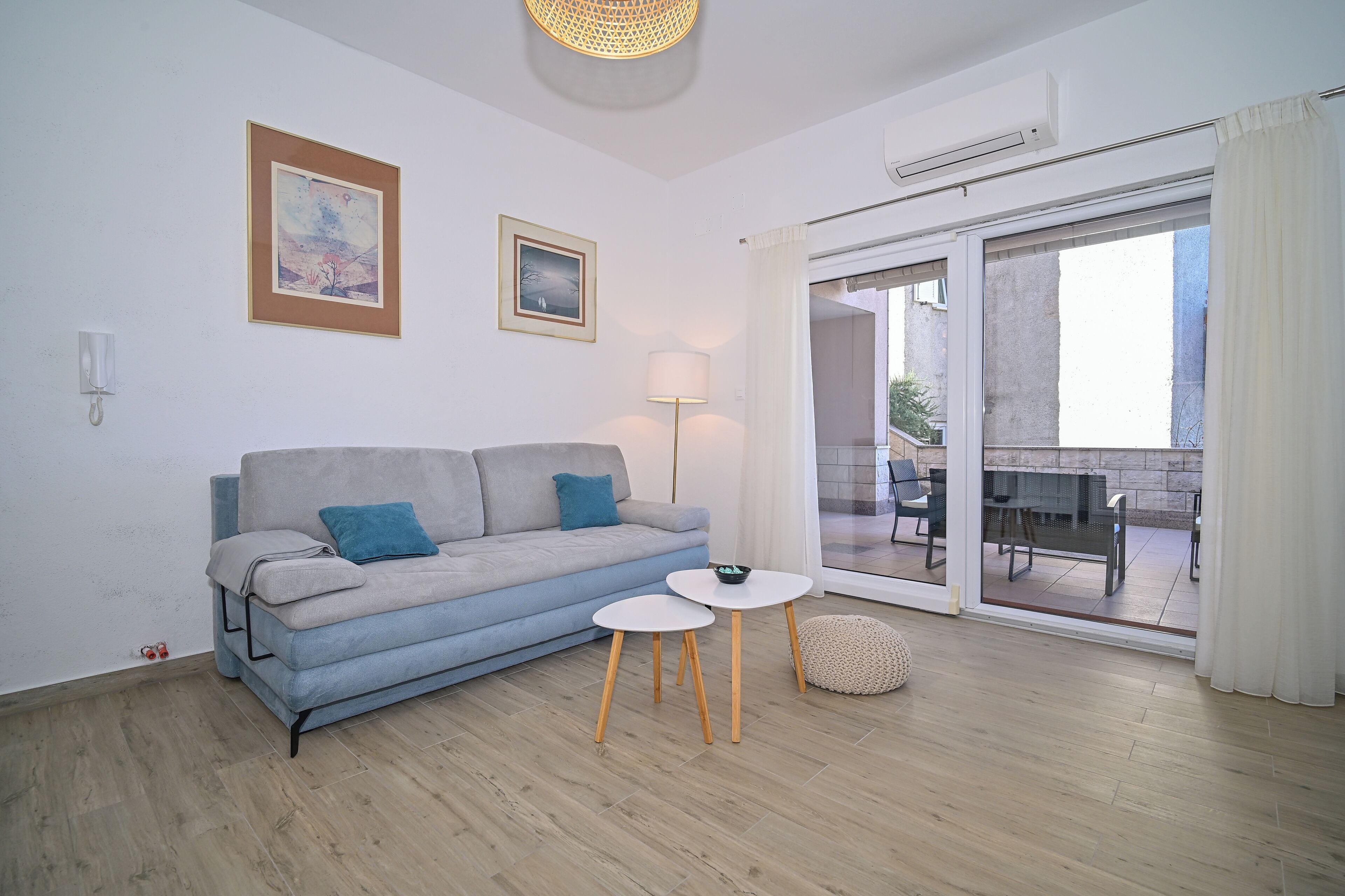 Uma sala de estar moderna com um sofá, uma mesinha, um abajur e vista para um pátio externo.