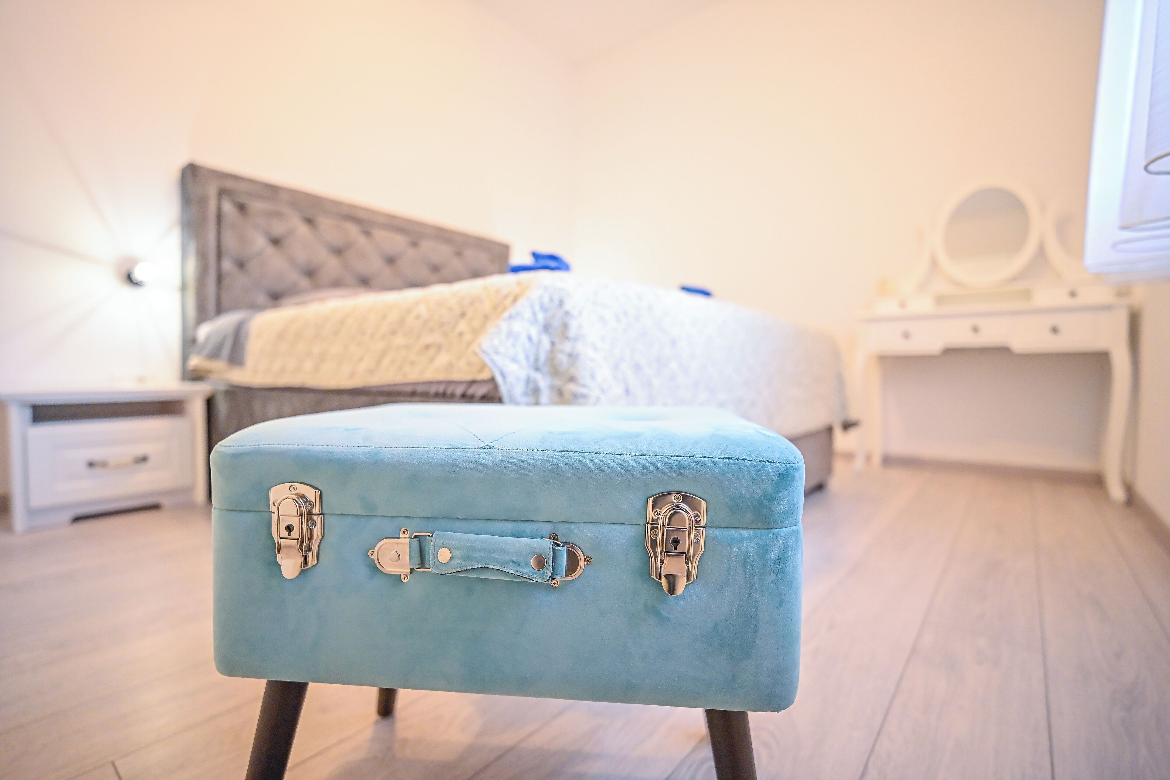 A bedroom with a bed, a bedside table, a dresser, and a blue suitcase.