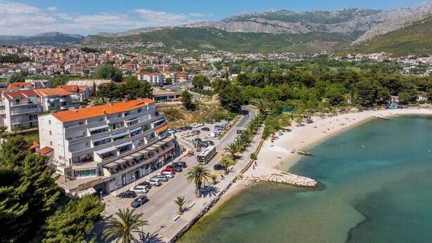 A coastal town with a beach, a road with parked cars, and a building with multiple floors. - AMI Apartment Strožanac (Podstrana)