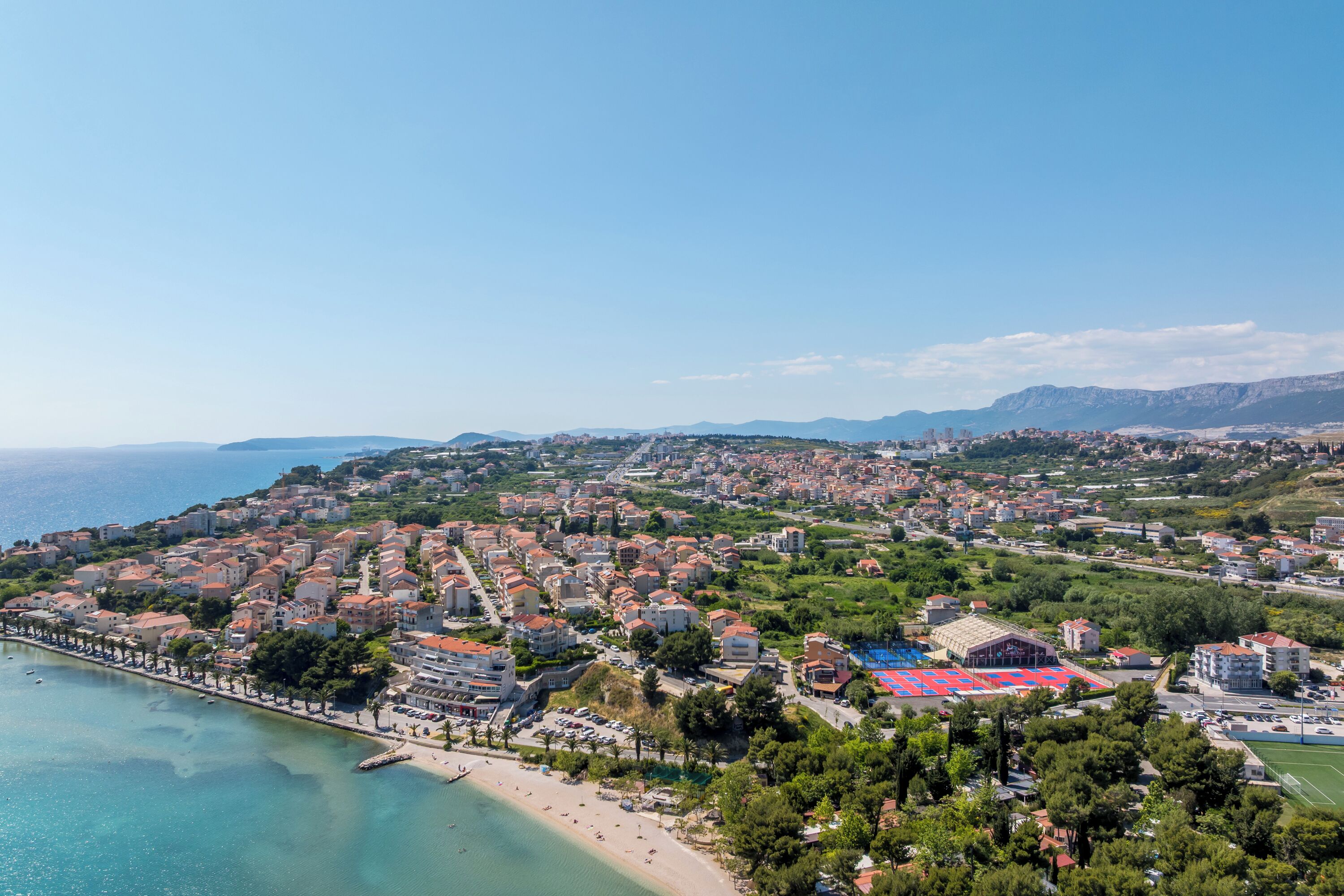 A coastal town with a beach, residential buildings, and a sports facility.