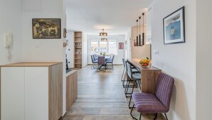 A modern kitchen with wooden cabinets, a dining area with a table and chairs, and a kitchen island with a fruit bowl. - Bells & Whistles, Comfortable Condo (Split)
